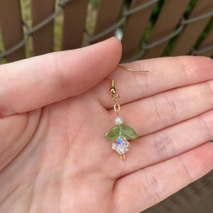 May include: Gold dangle earrings with a green glass flower and a white pearl bead.