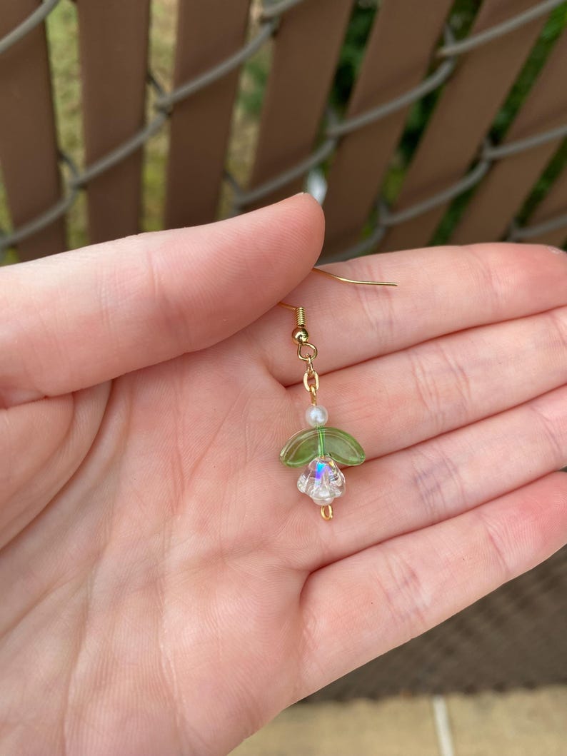 May include: Gold dangle earrings with a green glass flower and a white pearl bead.