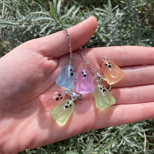 May include: A collection of colorful ghost charms in shades of blue, pink, orange, and green, each with black dot eyes. The charms are attached to a silver chain, creating a whimsical and spooky accessory.