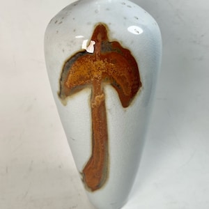 May include: A white ceramic vase with a brown abstract design. The vase has a narrow neck and a wide base.