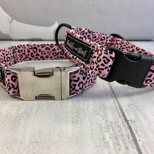 May include: Two pink and black leopard print dog collars with silver and black buckles. The collars are made by "Wibble and Boot".