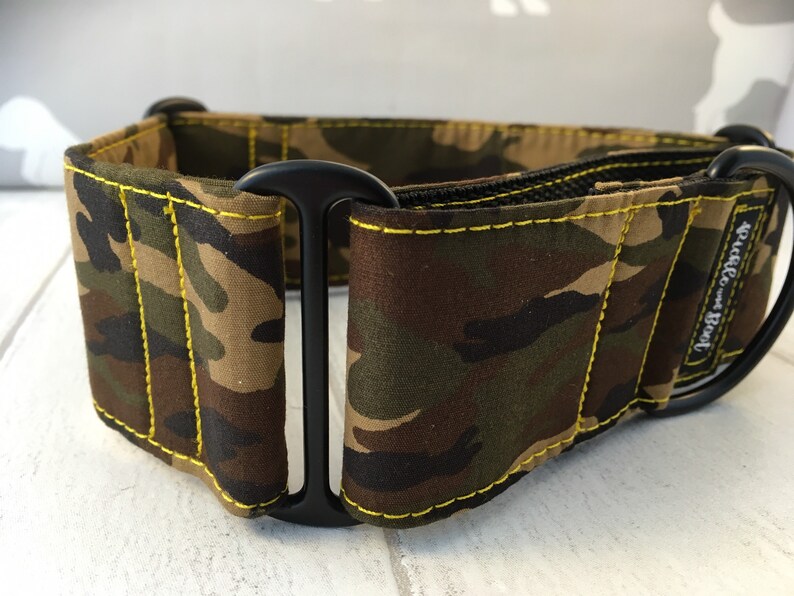 May include: A camouflage dog collar with yellow stitching and a black buckle. The collar is made by "Pickle-Butt" and is designed for dogs.