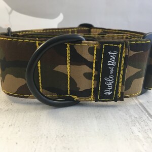 May include: A camouflage patterned dog collar with yellow stitching and a black metal D-ring. The collar has the text "Pickle and Boot" embroidered on it.