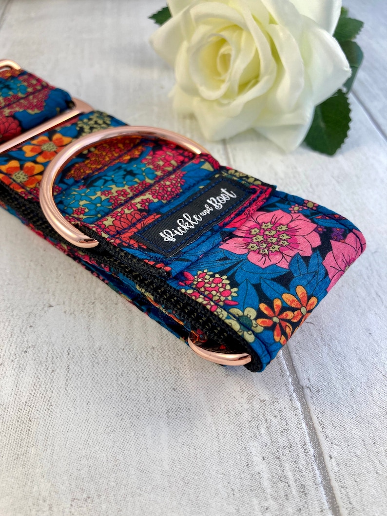 K&ouml;nnte beinhalten: Ein gemustertes Hundehalsband mit einem D-Ring und Beschl&auml;gen aus ros&eacute;goldfarbenem Metall. Das Halsband zeigt ein Blumenmuster in Rosa, Orange und Blau auf dunkelblauem Grund. Der Text "Pickle and Root" ist auf dem Halsband zu sehen.