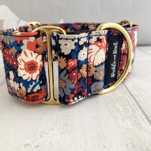 May include: A floral patterned dog collar with a gold-colored metal buckle and hardware. The collar features a navy blue background with red, white, and blue flowers. The text "Pickle and Boot" is visible on a navy blue label.