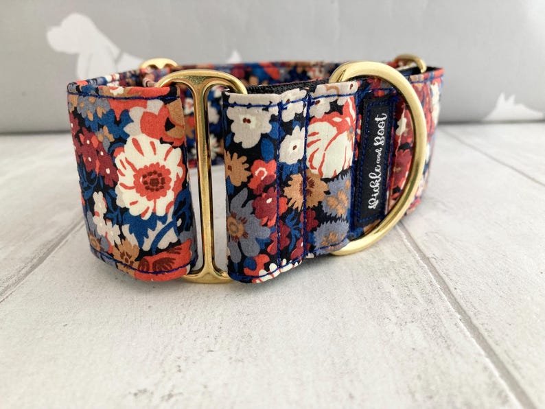 May include: A floral patterned dog collar with a gold-colored metal buckle and hardware. The collar features a navy blue background with red, white, and blue flowers. The text "Pickle and Boot" is visible on a navy blue label.
