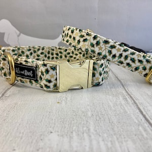 Op de afbeelding: Twee hondenhalsbanden met een witte achtergrond en een patroon van groene en gouden bladeren. De halsbanden hebben gouden beslag en de grotere halsband heeft de tekst "Paw and Boot" erop.