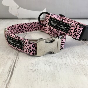 May include: Two pink and black leopard print dog collars with silver buckles. The collars have the text "Pickle and Boot" on them.