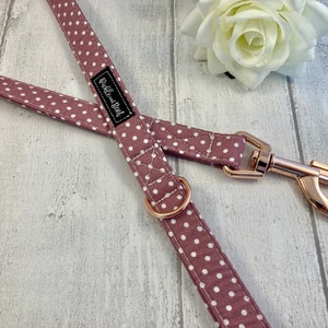 May include: Mauve and white polka dot dog lead with rose gold coloured metal fittings. The lead has a metal clasp and a matching metal ring. The brand name "Rubble and Flint" is printed on a black label.