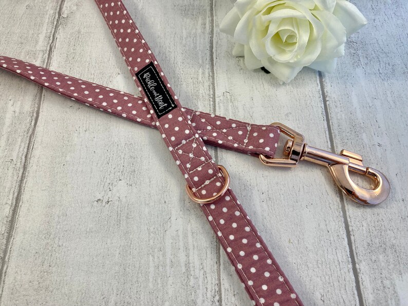 May include: Mauve and white polka dot dog lead with rose gold coloured metal fittings. The lead has a metal clasp and a matching metal ring. The brand name "Rubble and Flint" is printed on a black label.