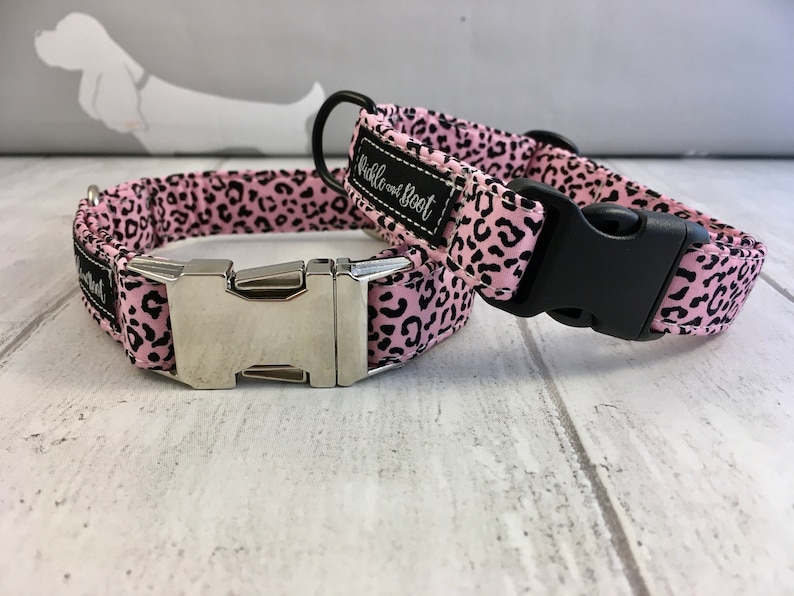 May include: Two pink and black leopard print dog collars with silver and black buckles. The collars are made by "Wibble and Boot".