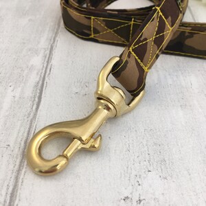 May include: A brown and green camouflage dog leash with yellow stitching and a gold metal clasp.