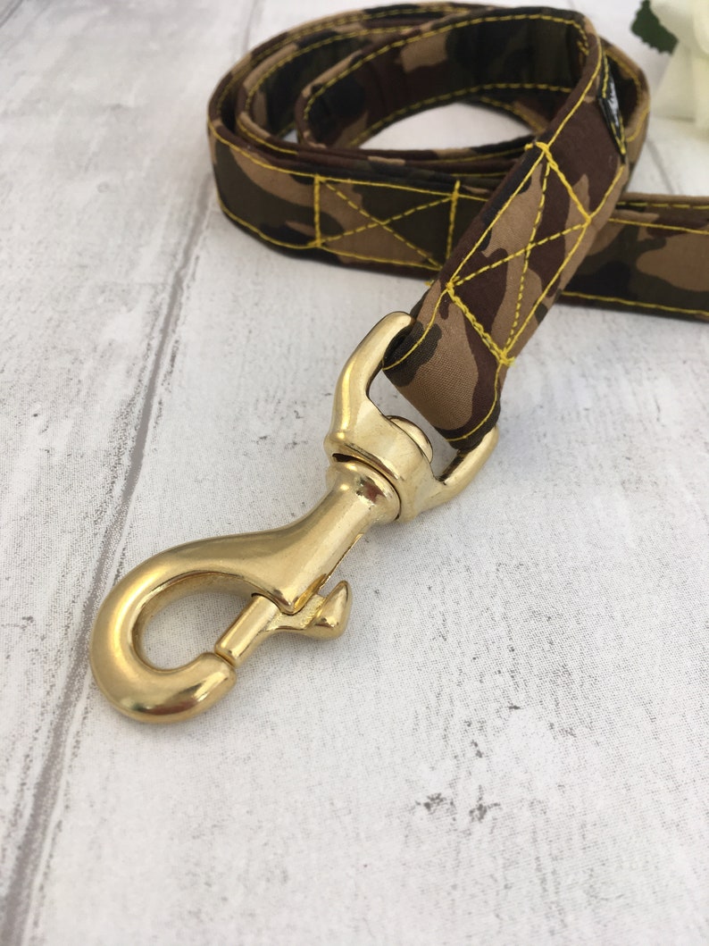 May include: A brown and green camouflage dog leash with yellow stitching and a gold metal clasp.