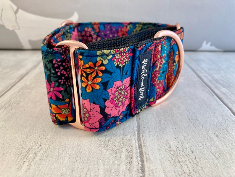 K&ouml;nnte beinhalten: Ein floraler Hundehalsband mit marineblauem Hintergrund und rosa, orangefarbenen und blauen Blumen. Das Halsband hat ros&eacute;goldfarbene Hardware und eine schwarze Innenseite. Das Etikett lautet "Pickle and Boot".