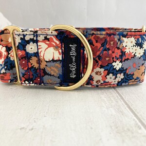 May include: A floral dog collar with a navy blue base, featuring a pattern of red, white, and blue flowers. The collar has gold-colored hardware and a navy blue label with the text "Pickle and Boot".