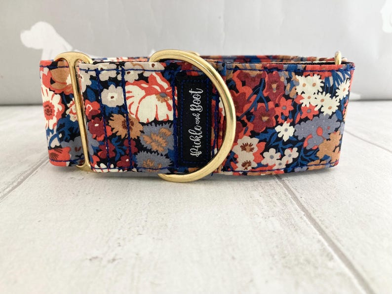 May include: A floral dog collar with a navy blue base, featuring a pattern of red, white, and blue flowers. The collar has gold-colored hardware and a navy blue label with the text "Pickle and Boot".