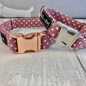 May include: Two dog collars in dusty rose fabric with white polka dots. One has a rose gold buckle, the other a silver buckle. Each collar features a black label with white text reading "Bubble and Boot".