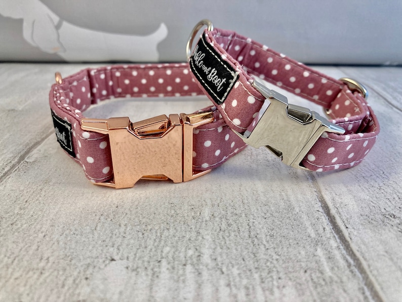 May include: Two dog collars in dusty rose fabric with white polka dots. One has a rose gold buckle, the other a silver buckle. Each collar features a black label with white text reading "Bubble and Boot".