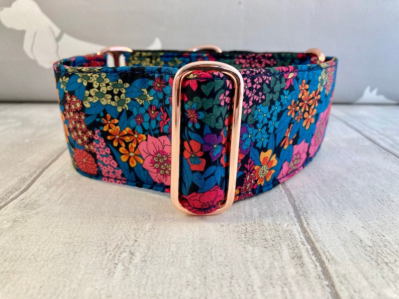 K&ouml;nnte beinhalten: Ein breites Hundehalsband mit einem Blumenmuster in Blau-, Rosa-, Orange- und Gr&uuml;nt&ouml;nen. Das Halsband hat ros&eacute;goldfarbene Beschl&auml;ge. Der Stoff ist dunkelblau mit einem farbenfrohen Blumendruck.