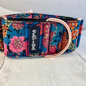 K&ouml;nnte beinhalten: Ein gemustertes Hundehalsband mit einem D-Ring und Beschl&auml;gen aus ros&eacute;goldfarbenem Metall. Das Halsband hat einen marineblauen Hintergrund mit rosa, blauen, orangefarbenen und gelben Blumen. Ein kleines marineblaues Etikett tr&auml;gt die Aufschrift "Pickle and Boot".