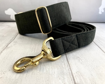 May include: A black dog collar and matching leash set. The collar features a gold-colored metal buckle, and the leash has a gold-colored metal clasp. The set is made of a dark gray fabric.