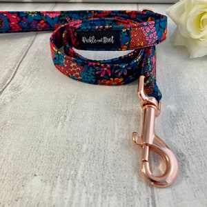 K&ouml;nnte beinhalten: Eine Hundeleine mit floralem Muster und einem ros&eacute;goldenen Karabinerhaken. Der Stoff hat einen marineblauen Hintergrund mit rosa, orangefarbenen und blauen Blumen. Das Etikett lautet "pickle and boot".