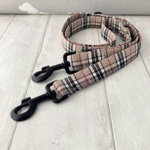 Puede incluir: Correa para perro con estampado de cuadros escoceses beige, negro y rojo. Cuenta con cierres metálicos negros para una sujeción segura. La tela presenta un diseño de cuadros clásico. Ideal para paseos caninos.