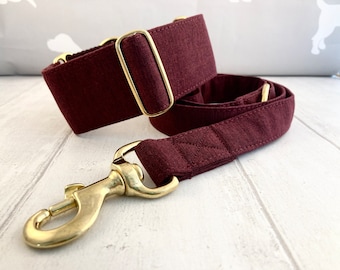 May include: A burgundy dog collar and matching leash set. The collar features a wide band with a gold-colored metal buckle. The leash has a gold-colored metal clasp. The set is made of a textured fabric.