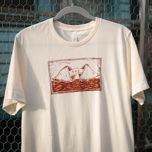 May include: A beige t-shirt with a red graphic print of two fortune cookies with the number 666 inside. The text "Lucky Number" is printed inside the fortune cookies.