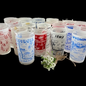 May include: A collection of vintage drinking glasses, each featuring a state's name and a map with illustrations of landmarks. The glasses have white backgrounds with red, blue, and black graphics. Some glasses have text like "Georgia", "Iowa", and "Wyoming".