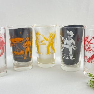 May include: Set of five vintage drinking glasses with retro illustrations. Designs include astronauts, a space scene, cowboys, a pirate, and a Native American figure. Each glass has a different color scheme.