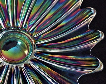Può includere: Una ciotola di vetro iridescente con un bordo a festoni e un cerchio centrale. La ciotola ha un effetto arcobaleno con sfumature di blu, verde, viola e rosa.