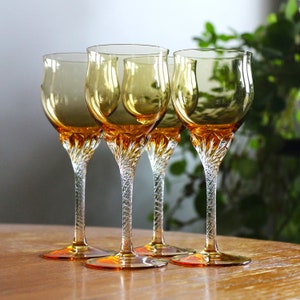 May include: Four amber-coloured wine glasses with a clear, twisted stem. The glasses have a wide bowl and a delicate, elegant design.