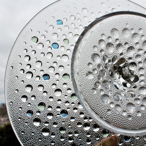 May include: Two clear glass plates with a textured surface. The top plate has a raised center and a pattern of small bubbles. The bottom plate has a pattern of larger bubbles.