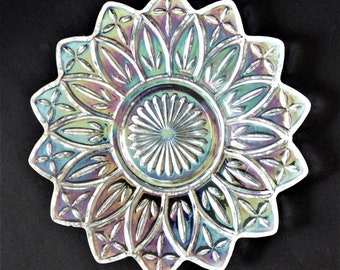 Può includere: Piatto in vetro iridescente con un design a stella. Il piatto presenta un'area circolare centrale con linee radiali ed è circondato da disegni a forma di petalo. I bordi hanno una forma smerlata. I colori virano dal blu al verde al viola.