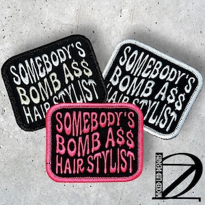 May include: Three embroidered patches with the text "SOMEBODY'S BOMB ASS HAIR STYLIST". One patch is black with white text, another is white with black text, and the third is pink with black text.