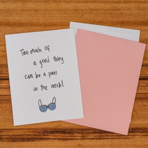 The card says ‘Too much of a good thing can be a pain in the neck!’.  Beneath is a small illustration of a large blue bra with pink trimming and a small pink bow.
——-
Inside: The inside of the card reads ‘Congrats on your new boobs!’.