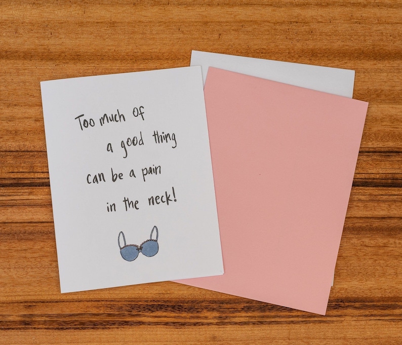 The card says ‘Too much of a good thing can be a pain in the neck!’.  Beneath is a small illustration of a large blue bra with pink trimming and a small pink bow.
——-
Inside: The inside of the card reads ‘Congrats on your new boobs!’.