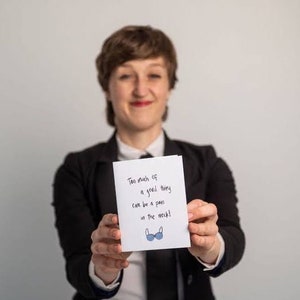 May include: A person holding a white card with the text "Too much of a good thing can be a pain in the neck!" and a blue bra illustration.