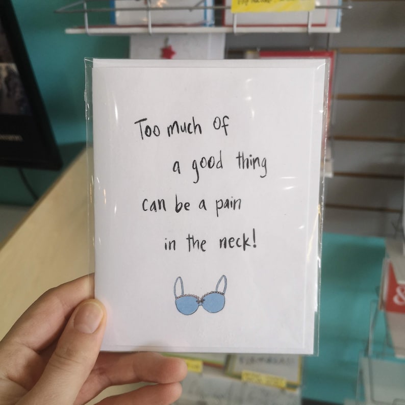 May include: A white card with black handwritten text that reads "Too much of a good thing can be a pain in the neck!" and a blue bra illustration.