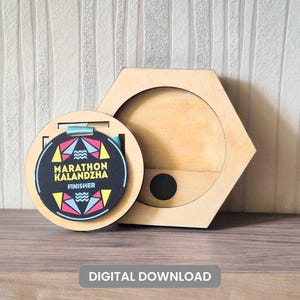 Può includere: Una medaglia di finisher di maratona in legno con un design geometrico in una custodia rotonda, accanto a una scatola esagonale in legno. La medaglia ha il testo "MARATHON KALANDZHA FINISHER". L'immagine include anche il testo "DIGITAL DOWNLOAD".