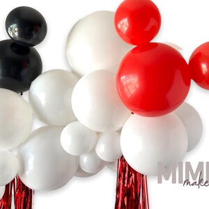 May include: A balloon arch featuring red, black, and white balloons arranged in the shape of Mickey Mouse ears. The arch is decorated with red streamers.