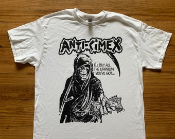 May include: White t-shirt with a black and white graphic print of a skeleton holding money. The text "ANTI-CIMEX" and "I'LL BUY ALL THE URANIUM YOU'VE GOT..." is printed on the shirt.