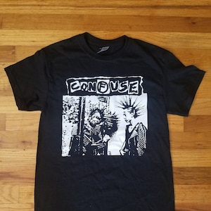 May include: Black t-shirt with a white graphic print of a band called "CONFUZE". The graphic features two people with spiky hair and leather jackets.