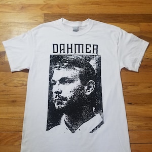 May include: White t-shirt with a black and white image of a man's face and the word "DAHMER" printed on the front.