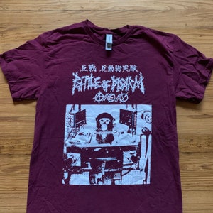 May include: A maroon t-shirt with a white graphic print of a monkey sitting at a desk with a computer monitor. The text on the shirt reads "Battle of Ypsilam" and "反戦 反動 物質 蔓延".