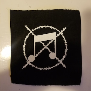 May include: Black fabric patch with a white musical note symbol inside a circle of barbed wire. The note is crossed out with two white lines.