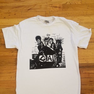 May include: White t-shirt with a black and white graphic print of a punk rock band. The band is standing in front of a brick wall and the graphic includes the text "GAG".