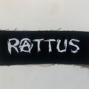 以下が含まれることがあります： 「RATTUS」という白い刺繍の文字が書かれた黒い布のパッチ。Aの代わりにアナーキーのシンボルが使われている。