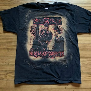 May include: Black t-shirt with a distressed graphic featuring the word "CONFUSE" above a red and black illustration and the words "NUCLEAR ADDICTS" below. The shirt has a faded, vintage look.